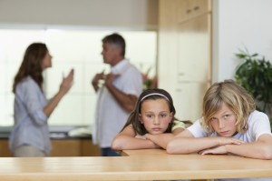 Sad looking siblings with arguing parents behind them